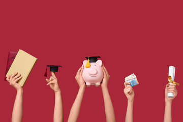 Female hands holding piggy bank with graduation cap, diploma and money on red background. Student...
