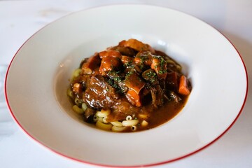 A plate of slow-cooked beef stew (boeuf bourguinon) with coquillette pasta at  a French bistro-style restaurant at Circular Quay in Sydney — New South Wales, Australia