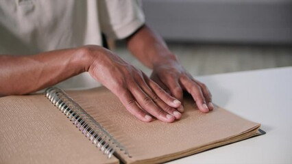 blind afro american man with poor eyesight reads a braille book runs his fingers across page in a cozy room