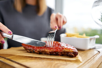 Lunch in a restaurant, a woman cuts Delicious Pork ribs. Full rack of ribs BBQ on wooden plate with french fries and salad