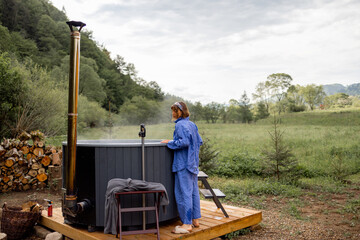 Woman rests in a house in the mountains, heats up a hot tub for bathing. Concept of recreation on...