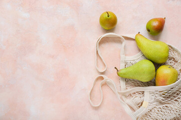 Mesh bag with ripe pears on pink table