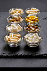 Vitamins pills in glass bowls on a stoneblack desk.