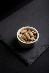 Vitamins tablets in a ceramic white small bowl from above on a blackstone desk on black background.