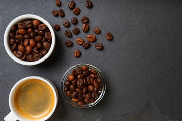 Porcelain cup of espresso coffee and aromatic roasted coffee beans in white bowl and glass bowl on black stone desk from above.