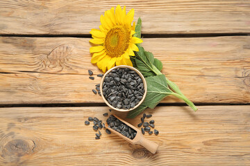 Beautiful sunflower and bowl with seeds on wooden background