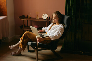 Relaxed woman sitting and watching something on her laptop with a cup of coffee in her hand