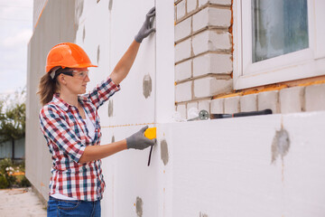 Insulation of the house with polyfoam. The worker is checking with the construction level the...