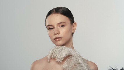 Pretty young brunette with natural makeup holding a white feather looking at the camera