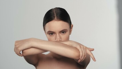 Young brunette female touching her hands smooth skin and looking at the camera