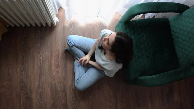 Psychology. Above view of anxiety woman is sitting near chair on floor in room and itching. Concept of loneliness and stress