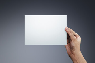 Woman hand holding a blank paper on gray background.