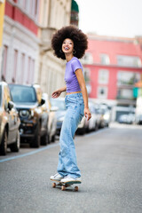 Smiling ethnic woman riding skateboard on road © photology1971