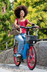 Delighted ethnic female riding electric bicycle on street in summer