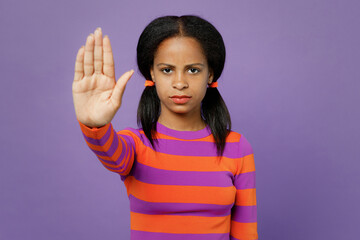 Little sad kid teen girl of African American ethnicity 15-16 years old wearing striped orange sweatshirt show stop gesture with palm isolated on plain purple background. Childhood lifestyle concept.