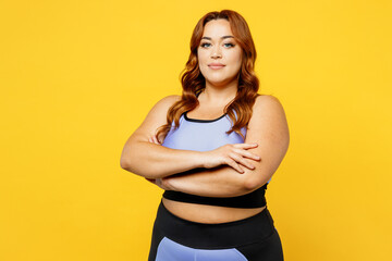 Young fun chubby overweight plus size big fat fit woman wear blue top warm up training hold hands crossde folded look camera isolated on plain yellow background studio home gym. Workout sport concept.