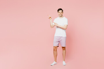Full body young man wearing white t-shirt casual clothes point index finger aside indicate on workspace area copy space mock up isolated on plain pastel light pink background studio Lifestyle concept