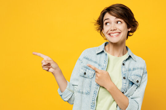 Young happy woman she wear green t-shirt denim shirt casual clothes point index finger aside indicate on workspace area copy space mock up isolated on plain yellow background studio Lifestyle concept