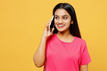 Young happy Indian woman wearing pink t-shirt casual clothes talking speak on mobile cell phone...