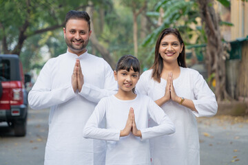 Indian couple his with daughter doing namaste or welcome gesture.