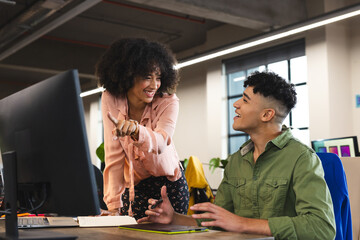 Happy diverse female and male colleagues in discussion at computer in office