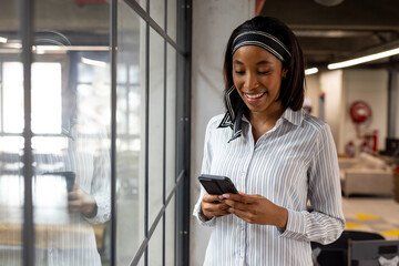 African american businesswoman using a smartphone near a window at modern office, copy space