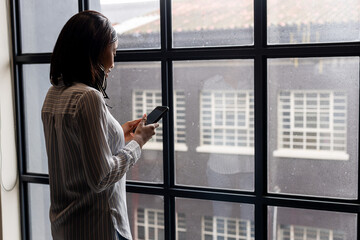 African american businesswoman using a smartphone near a window at modern office, copy space