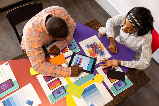 Overhead view of diverse designers discussing over digital tablet at office, copy space - Powered by Adobe