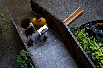 Overhead view of diverse businesspeople discussing over a laptop on the stairs at office, copy space