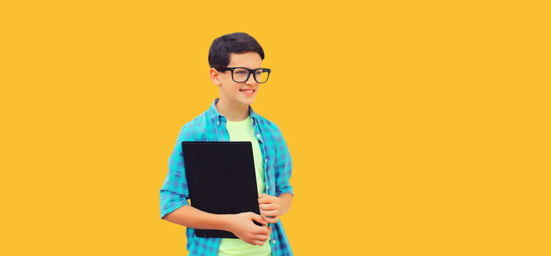 Portrait of happy smiling teenager boy in eyeglasses with folder or book on yellow background