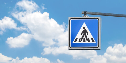 Blue, white and black pedestrian crossing sign on the sky background. Copy space for text and...