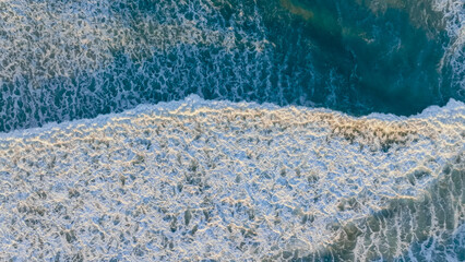 Waves crashing onto the sandy shoreline during the golden hour at a coastal beach in the early evening