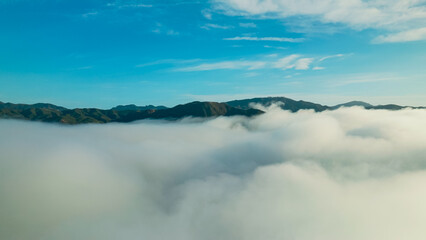 Mountain peaks emerge through a blanket of clouds beneath a clear blue sky during the early morning...