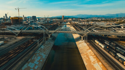 Fototapeta premium Urban landscape showing train tracks and bridges alongside a waterway in a bustling city at sunset
