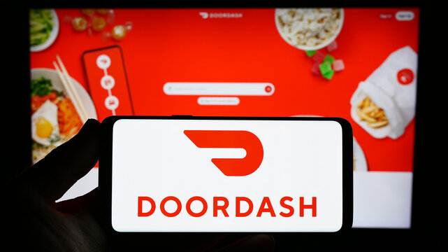 Stuttgart, Germany - 07-25-2023: Person holding smartphone with logo of US food delivery company DoorDash Inc. on screen in front of website. Focus on phone display.
