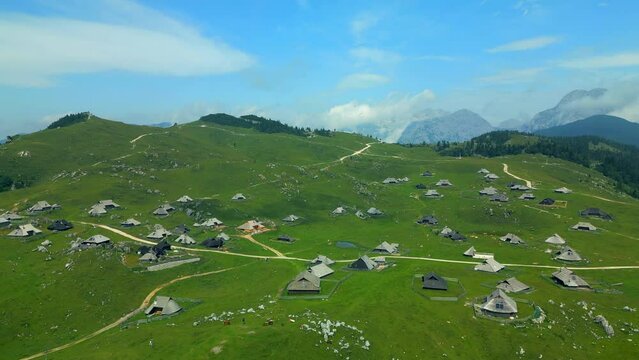 Velika Planina or Big Pasture Plateau in the Kamnik, Alps, Slovenia. Mountain cottage hut or house on green hill. Alpine meadow landscape. Eco food production, aerial view.