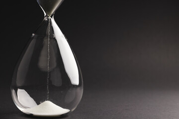 Close up of hourglass with white sand and copy space on black background