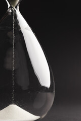 Close up of hourglass with white sand and copy space on black background
