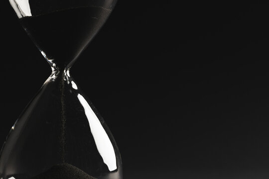 Close up of hourglass with black sand and copy space on black background