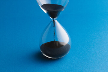 Close up of hourglass with black sand and copy space on blue background
