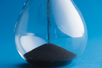 Close up of hourglass with black sand and copy space on blue background