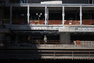 Construction workers at an unfinished building, part of a construction project for a major infrastructure project. Daylight casts strong, dramatic shadows.