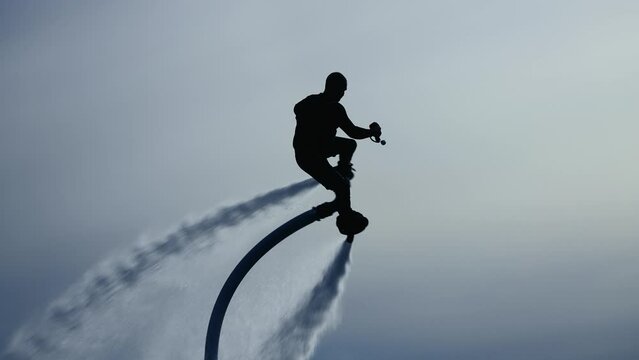 Water extreme. Flyboarder performs tricks over water. Silhouette of an unrecognizable male flyboarder