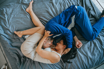 Top view on kissing young couple laying on bed at home. Lovers embracing each other at bedroom. Romance concept. Husband kissing wife  at home. Relationship, love.