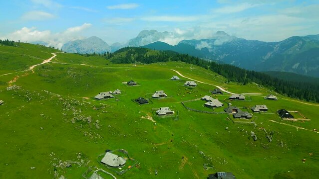 Velika Planina or Big Pasture Plateau in the Kamnik, Alps, Slovenia. Mountain cottage hut or house on green hill. Alpine meadow landscape. Eco food production, aerial view.