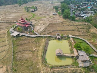 Bird's eye view of the Bamboo Bridge in Pai, Thailand with a traditional hut in the middle and rice fields around it.