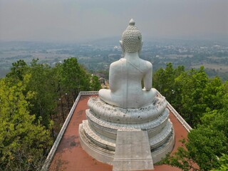 The impressive Big Buddha statue in Pai, Thailand high up on a tree covered hill taken from behind with the valley in the background.