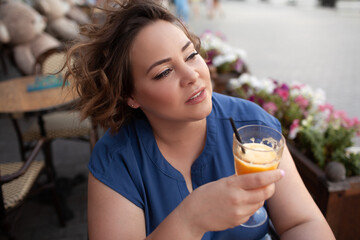 Beautiful young woman sit in cafe with glass of cooly drink. Plus size woman  drink red juice and smiling