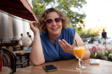 Beautiful young woman sit in cafe with glass of cooly drink. Plus size woman  drink red juice and smiling