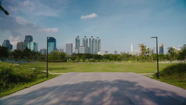 Camera moves forward along an urban landscape with skyscrapers in a green empty park. Modern downtown view from a city cental park in Bangkok
